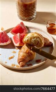 food, drink and eating concept - glass of coffee, honey, croissant and grapefruit on plate for breakfast. glass of coffee, croissant and grapefruit on table