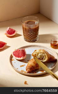 food, drink and eating concept - glass of coffee, honey, croissant and grapefruit on plate for breakfast. glass of coffee, croissant and grapefruit on table