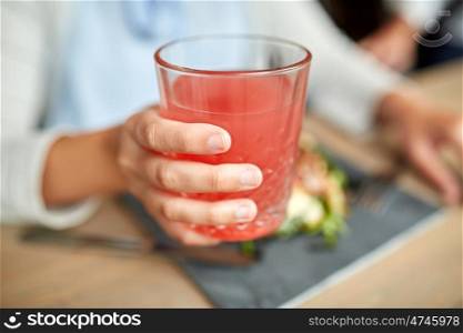 food, drink, eating and people concept - hand of woman with glass of juice and salad at restaurant