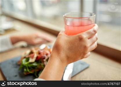food, drink, eating and people concept - hand with glass of juice and salad at restaurant