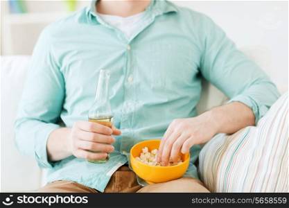 food, drinks, relax, leisure and people concept - close up of man with popcorn and beer sitting on couch at home