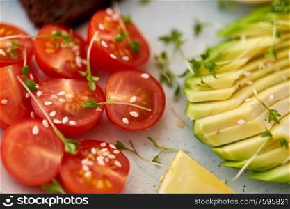 food, eating and breakfast concept - close up of cherry tomatoes and sliced avocado with thyme and sesame on ceramic plate. cherry tomatoes and sliced avocado with thyme