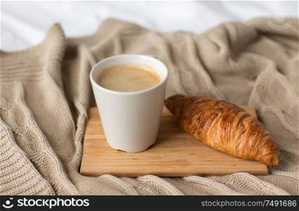 food, eating and breakfast concept - cup of coffee and croissant on bed or blanket at cozy home. cup of coffee and croissant on bed or blanket