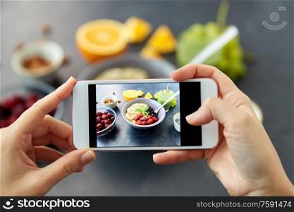 food, eating and breakfast concept - hand of woman taking picture of cereals in bowl with fruits, berries and juice with smartphone. hands taking picture of breakfast with smartphone