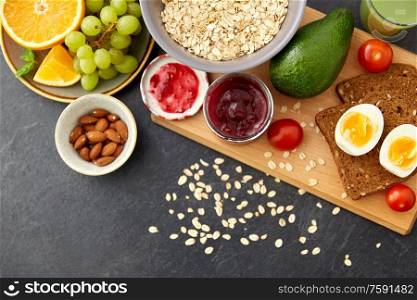 food, eating and breakfast concept - oatmeal cereals in bowl, fruits, almond nuts, jam and toast bread on slate stone table. oatmeal, fruits, toast bread, egg, jam and milk