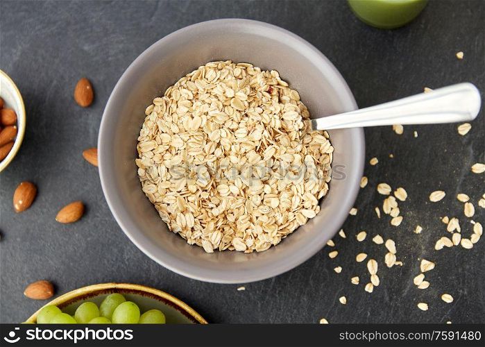 food, eating and breakfast concept - raw oatmeal cereals in bowl with spoon on slate stone table. oatmeal cereals in bowl with spoon