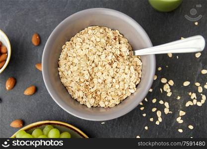 food, eating and breakfast concept - raw oatmeal cereals in bowl with spoon on slate stone table. oatmeal cereals in bowl with spoon