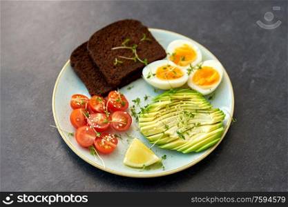 food, eating and breakfast concept - toast bread with cherry tomatoes, avocado, eggs and greens on ceramic plate. avocado, eggs, toast bread and cherry tomato