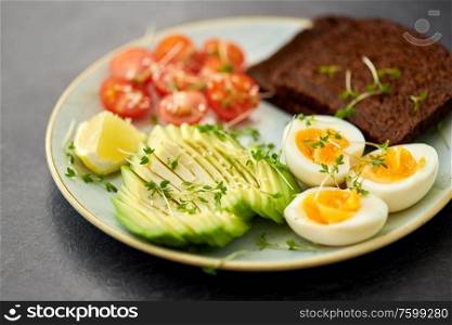 food, eating and breakfast concept - toast bread with cherry tomatoes, avocado, eggs and greens on ceramic plate. avocado, eggs, toast bread and cherry tomato