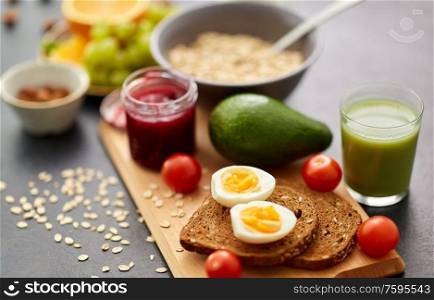food, eating and breakfast concept - toast bread with eggs, cherry tomatoes, avocado and glass of juice on wooden cutting board. toast bread, eggs, avocado, jam, tomato and juice