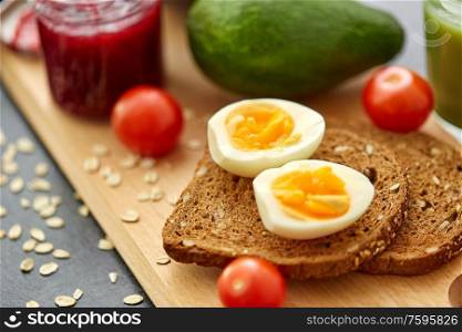 food, eating and breakfast concept - toast bread with eggs, cherry tomatoes, avocado and greens on wooden cutting board. toast bread with eggs, cherry tomatoes and avocado