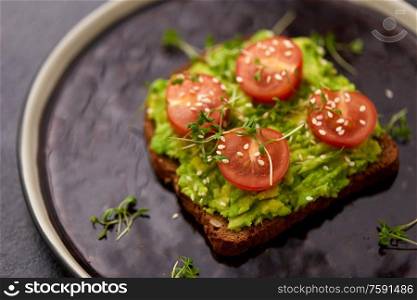 food, eating and breakfast concept - toast bread with mashed avocado, cherry tomatoes and greens on ceramic plate. toast bread with mashed avocado and cherry tomato
