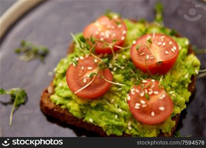 food, eating and breakfast concept - toast bread with mashed avocado, cherry tomatoes and greens on ceramic plate. toast bread with mashed avocado and cherry tomato