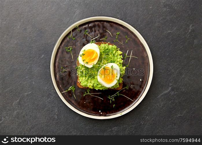 food, eating and breakfast concept - toast bread with mashed avocado, eggs and greens on ceramic plate. toast bread with mashed avocado and eggs