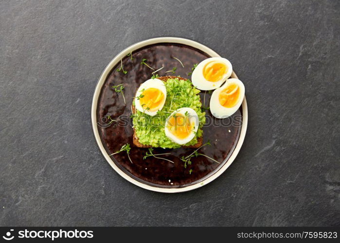 food, eating and breakfast concept - toast bread with mashed avocado, eggs and greens on ceramic plate. toast bread with mashed avocado and eggs