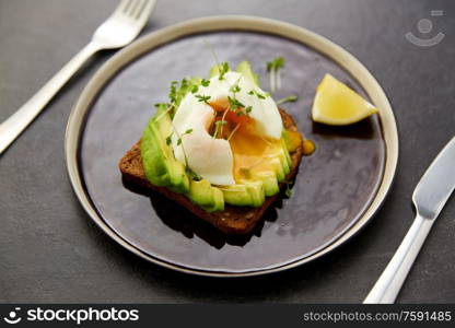 food, eating and breakfast concept - toast bread with sliced avocado, pouched egg and greens on ceramic plate with fork and knife. toast bread with sliced avocado and pouched egg