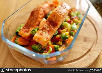 food, eating and culinary concept - close up of salmon fish with vegetables in baking dish on kitchen table at home. salmon fish in baking dish on kitchen table