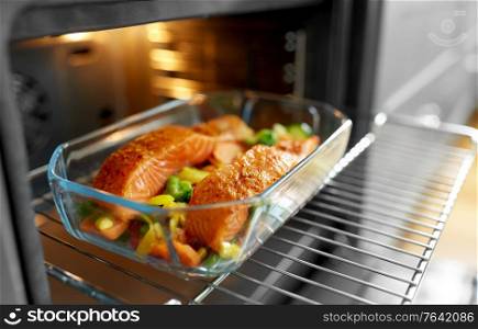 food, eating and culinary concept - salmon fish with vegetables cooking in baking dish in oven at home. food cooking in baking dish in oven at home