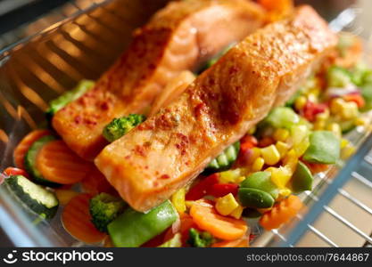 food, eating and culinary concept - salmon fish with vegetables cooking in baking dish in oven at home. food cooking in baking dish in oven at home