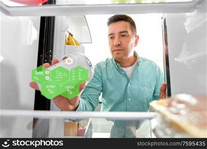 food, eating and diet concept - middle-aged man taking yoghurt from fridge at kitchen over nutritional value chart. man taking food from fridge at kitchen
