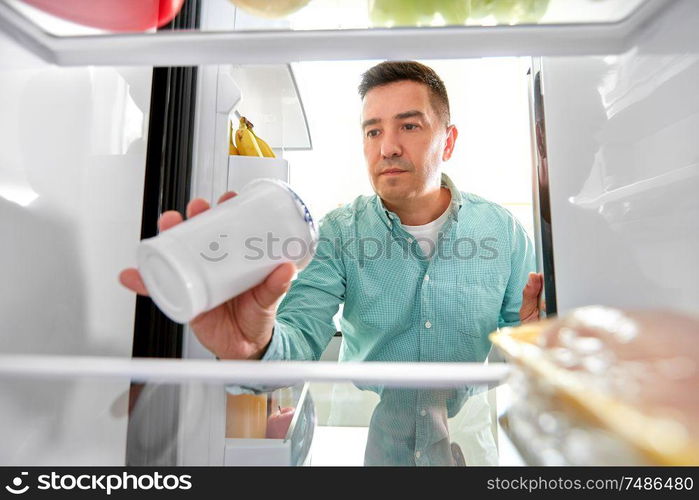 food, eating and diet concept - middle-aged man taking yoghurt from fridge at kitchen. man taking food from fridge at kitchen