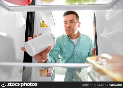 food, eating and diet concept - middle-aged man taking yoghurt from fridge at kitchen. man taking food from fridge at kitchen