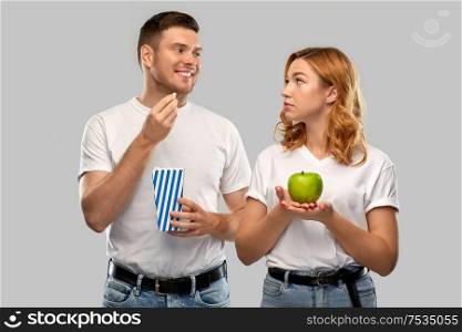 food, eating and diet concept - portrait of happy couple in white t-shirts with popcorn and green apple over grey background. couple in white t-shirts with popcorn and apple
