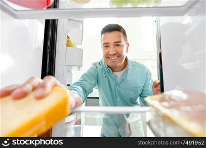 food, eating and diet concept - smiling middle-aged man taking cheese from fridge at kitchen. man taking food from fridge at kitchen