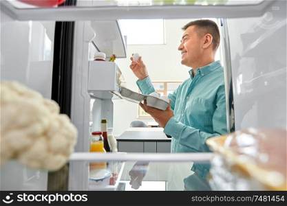 food, eating and diet concept - smiling middle-aged man taking eggs from fridge at kitchen. man taking eggs from fridge at kitchen