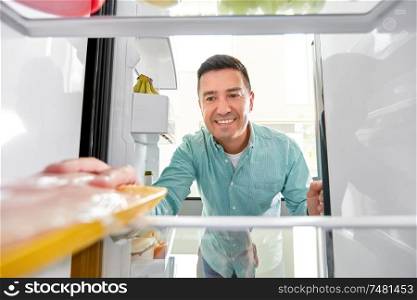 food, eating and diet concept - smiling middle-aged man taking meat from fridge at kitchen. man taking food package from fridge at kitchen