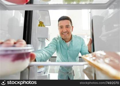 food, eating and diet concept - smiling middle-aged man taking yoghurt from fridge at kitchen. man taking food from fridge at kitchen