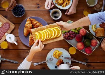 food, eating and family concept - group of people having breakfast and sharing orange at table. group of people having breakfast at table