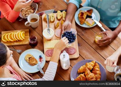 food, eating and family concept - group of people sharing blueberries for breakfast at wooden table. people having breakfast at table with food
