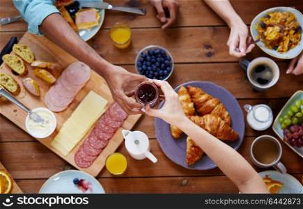 food, eating and family concept - group of people sharing jam for breakfast at wooden table. people having breakfast at table with food