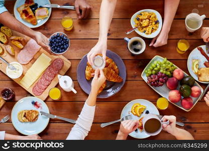 food, eating and family concept - group of people sharing milk or cream for breakfast at wooden table. people having breakfast at table with food