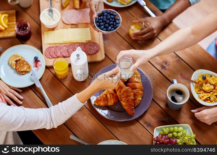 food, eating and family concept - group of people sharing milk or cream for breakfast at wooden table. people having breakfast at table with food