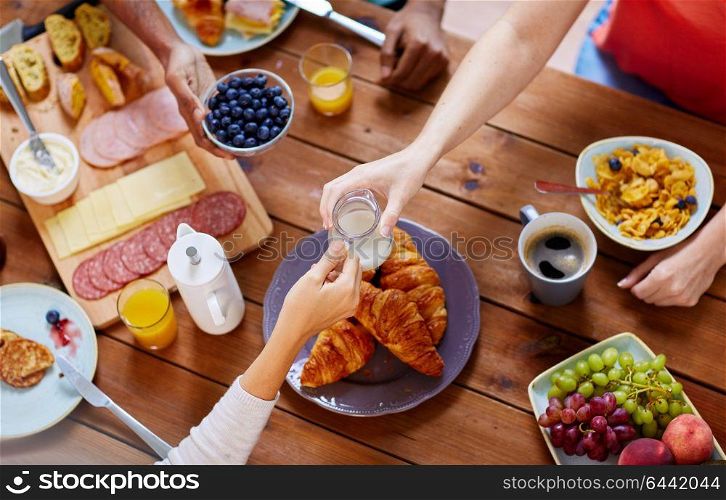 food, eating and family concept - group of people sharing milk or cream for breakfast at wooden table. people having breakfast at table with food