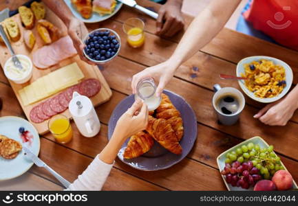 food, eating and family concept - group of people sharing milk or cream for breakfast at wooden table. people having breakfast at table with food