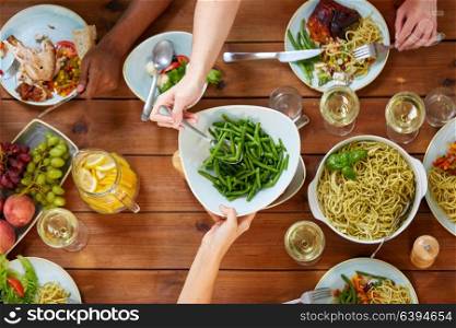 food, eating and leisure concept - people with green beans having dinner. people at table with food eating green beans