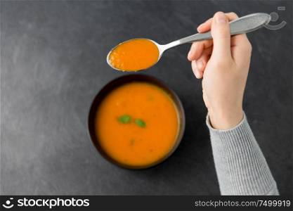 food, eating and new nordic cuisine concept - close up of hands with bowl of pumpkin cream soup and spoon on stone table. hands with bowl of pumpkin cream soup on table