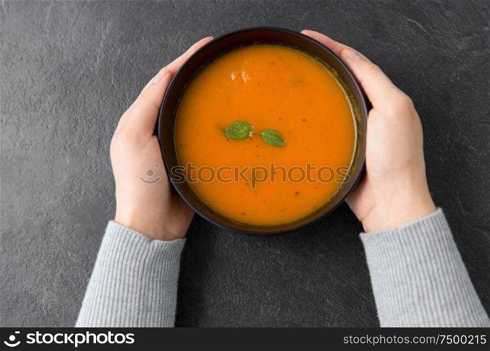 food, eating and new nordic cuisine concept - close up of hands with bowl of pumpkin cream soup on stone table. hands with bowl of pumpkin cream soup on table