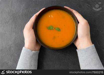 food, eating and new nordic cuisine concept - close up of hands with bowl of pumpkin cream soup on stone table. hands with bowl of pumpkin cream soup on table