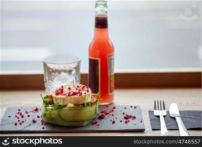 food, eating and object concept - goat cheese salad with vegetables, bottle of drink, glass with ice and cutlery at restaurant or cafe