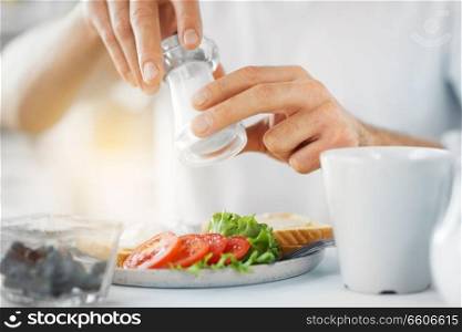 food, eating and people concept - close up of male hands seasoning breakfast by salt mill. close up of male hands seasoning food by salt mill