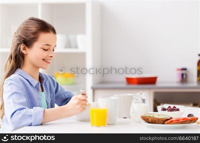 food, eating and people concept - happy girl having breakfast at home kitchen. happy girl having breakfast at home