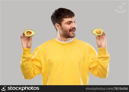 food, eating and people concept - smiling young man in yellow sweatshirt with avocado over grey background. happy young man in yellow sweatshirt with avocado