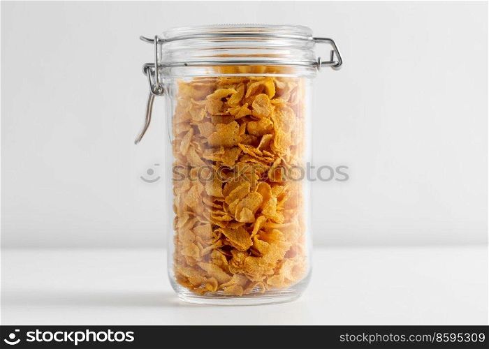 food, eating and storage concept - close up of jar with corn flakes on white background. close up of jar with corn flakes on white table
