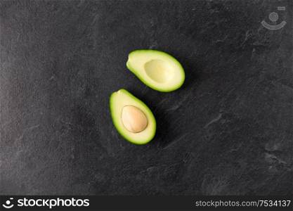 food, eating and vegetable concept - close up of cut avocado with bone on slate stone background. close up of ripe avocado on slate stone background