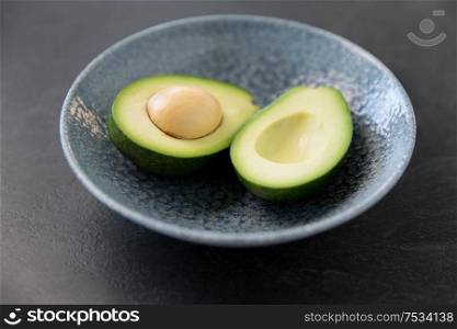 food, eating and vegetable concept - close up of cut avocado with bone in ceramic bowl on slate stone background. close up of ripe avocado with bone in ceramic bowl