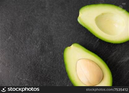 food, eating and vegetable concept - close up of cut avocado with bone on slate stone background. close up of ripe avocado on slate stone background